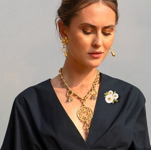 Detail of vintage gold chain necklace with daisy brooch on dark blue fabric background