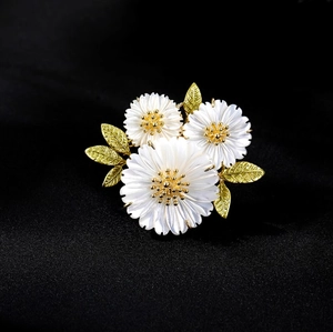 Elegant daisy flower brooch with pearly petals and gold leaves on dark fabric