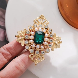 Vintage royal style gold brooch with emerald crystal and white pearls on white background
