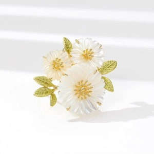 Exquisite white daisy flower brooch with gold accents and green leaves on white background