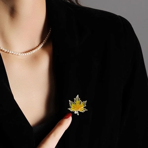 Macro detail of enamel maple leaf brooch with gold trim on black velvet suit lapel