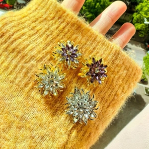 Makroaufnahme von 3D-Kristallblumen-Broschen mit Strasssteinen auf gelbem Strick