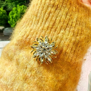 Eleganter goldener Blumenanstecker mit Kristall-Strass auf einem gelben Strickpullover