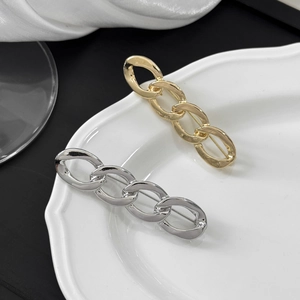 Minimalist gold and silver polished metal chain brooches on a white ceramic plate
