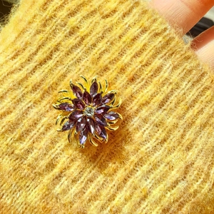 Detailaufnahme einer lila Marquise-Brosche auf einem gelben Strickstoffhintergrund
