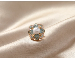 Détail macro d'une broche fleur vintage avec pétales émaillés et perle sur de la soie