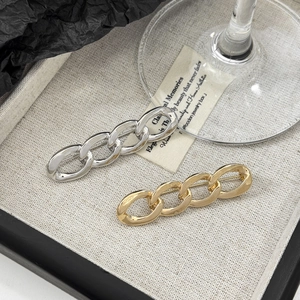 Detailed view of gold and silver cuban link chain brooches on a textured beige tray