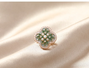 Détail macro d'une broche fleur vintage avec émail vert, perles et cristaux sur soie
