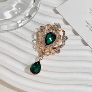Detailed close-up of vintage gold brooch with pear-shaped green crystal and rhinestones