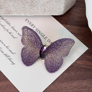 Dettaglio di spilla a farfalla viola ricamata a mano con una gemma viola sfaccettata
