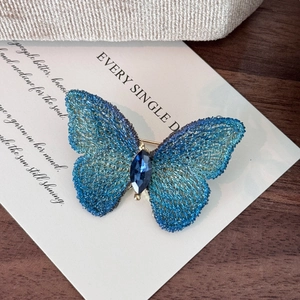 Dettaglio macro della spilla a farfalla blu ricamata a mano con gemma incastonata