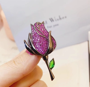 Detailed view of luxury rose brooch with pink zircons and green crystal leaf