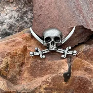 Vintage pirate skull with crossed swords brooch in antique silver finish on a rock background