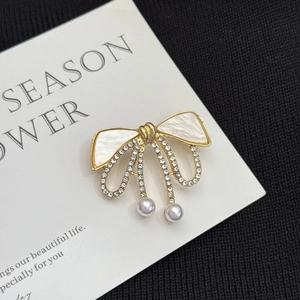 Détail d'une broche nœud dorée avec émail blanc, strass et pendentifs en perles