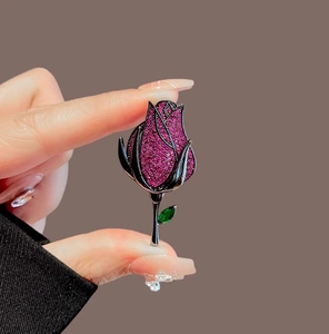 Detail of luxury rose brooch with magenta crystals and green emerald leaf accent