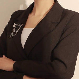 Close-up of a silver Saturn planet brooch with hanging chains on a black suit jacket