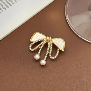 Broche nœud élégante en finition dorée avec strass et pendentifs en perles blanches