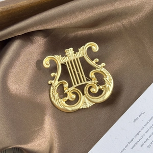 Detailed close-up of a matte gold lyre harp brooch on elegant dark satin fabric