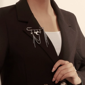Silver safety pin brooch with star and moon charms and metallic tassels on black blazer