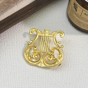 Vintage matte gold harp brooch with intricate lyre detailing in a classic art style