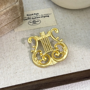 Matte gold lyre harp brooch with vintage embossed details on textured background