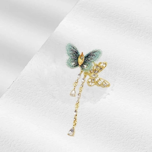 Makro-Detail der Stoff-Schmetterlingsbrosche mit goldenen Quasten und smaragdgrünen Texturen