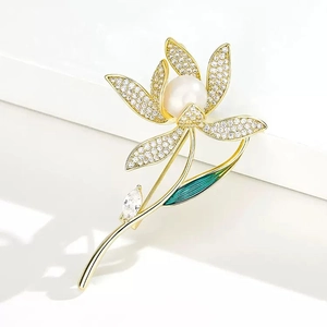 Close-up of golden enamel flower brooch with zircons, white pearl and green leaf detail