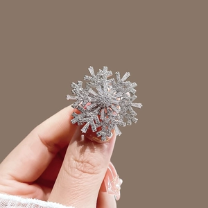 Luxurious silver snowflake brooch with sparkling crystals held by a model on brown background