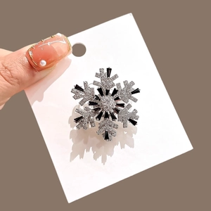 Close-up of a silver snowflake brooch with black and clear rhinestones on a card