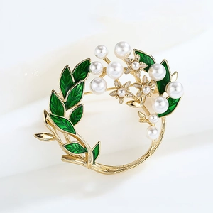 Detailed view of enamel flower wreath brooch with green leaves and pearls on gold metal