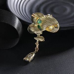 Elegant gold lotus brooch with green petals and a crystal drop pendant on black silk