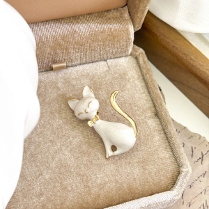 Elegant white enamel cat brooch with gold accents resting in a velvet jewelry box