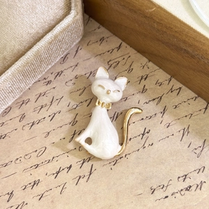 Elegant white enamel cat brooch with gold bow knot on vintage calligraphy background