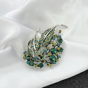 Close-up of vintage silver leaf brooch with emerald and yellow rhinestones on silk