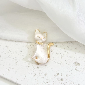 Detailed close-up of a white enamel cat brooch with elegant gold trim and bow detail