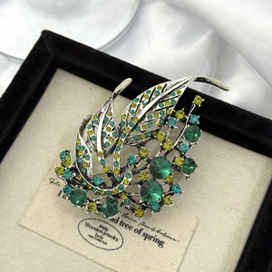 Close-up of hollow leaf brooch with emerald green crystals on vintage silver base