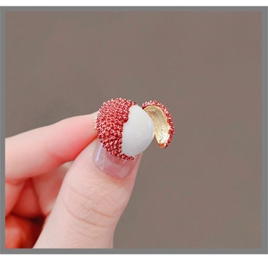 Nahaufnahme einer kleinen Litschi-Brosche in der Hand mit feinen Texturen und Goldakzenten