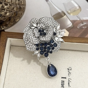 Elegant silver rose brooch with sparkling white rhinestones and deep blue crystal pendant