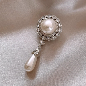 Close-up of vintage pearl brooch with teardrop pendant on champagne silk fabric