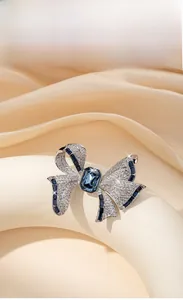 Détail de broche nœud argentée avec pierre bleue taille émeraude sur soie champagne