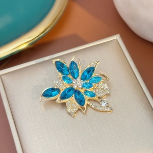 Vue détaillée d'une broche fleurie avec cristaux bleu foncé et strass sur un coffret à bijoux
