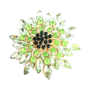 Elegant magnolia flower brooch with green crystals and gold base on white background