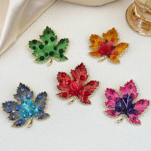 Five vintage enamel maple leaf brooches with gradient colors and rhinestones on beige silk
