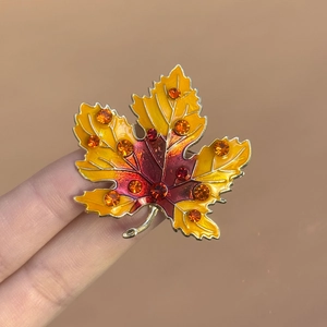 Macro view of gradient enamel maple leaf brooch with sparkling crystals on gold metal