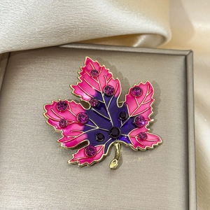 Detailed close-up of a maple leaf brooch with enamel gradient and purple rhinestones