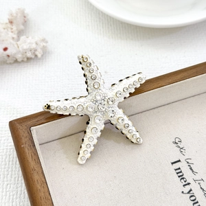 Starfish brooch with white enamel and sparkling rhinestones on a wooden frame