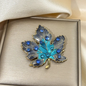 Macro shot of maple leaf brooch featuring blue gradient enamel and sparkling rhinestones