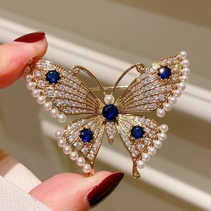 Handheld butterfly brooch with pearls, white rhinestones, and blue gemstones on gold metal