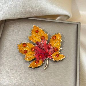 Detail of maple leaf brooch with enamel gradient and rhinestones on satin