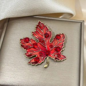 Detail of red enamel maple leaf brooch with gold edges and sparkling crystals